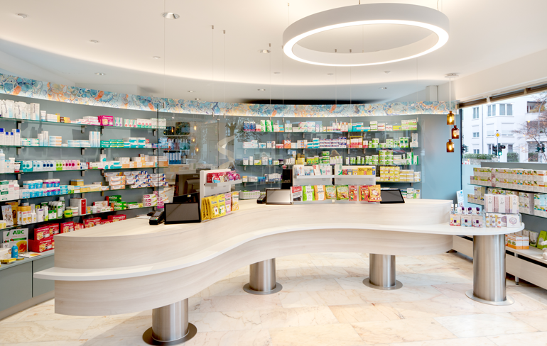 Moderne und frisch renovierte Innenansicht der Rotenbühl Apotheke mit einer stilvollen, geschwungenen Theke, hellen LED-Beleuchtungen und einem gut sortierten Medikamentenangebot.